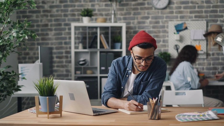 Masa başında not defterine yazı yazan bir kişi